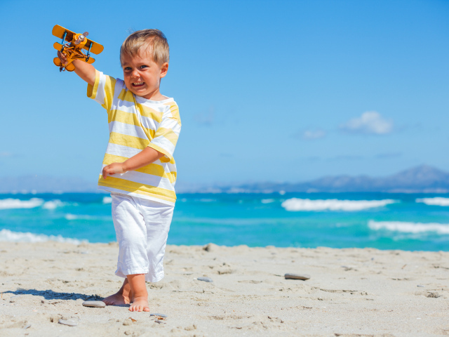 Маленький мальчик на пляже с игрушечным самолетом в руках