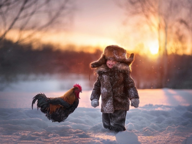 Маленький мальчик с петухом на снегу зимой
