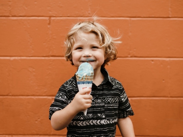 Маленький мальчик с мороженым в руках у стены