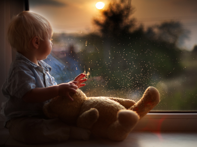Маленький мальчик с игрушкой у окна