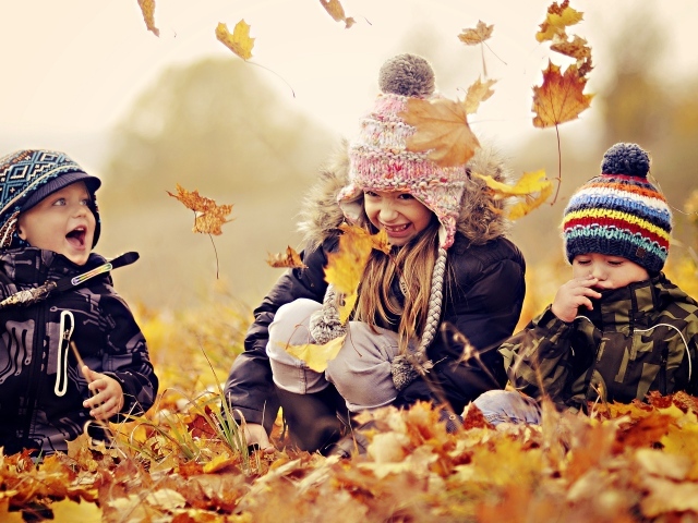 Маленькие дети играют на опавшей желтой листве осенью