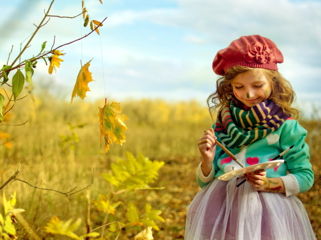 Маленькая девочка рисует красками на листьях осенью 