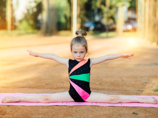 Маленькая девочка гимнастка сидит на шпагате 