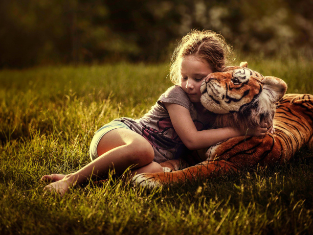 Маленькая девочка обнимает игрушечного тигра на зеленой траве