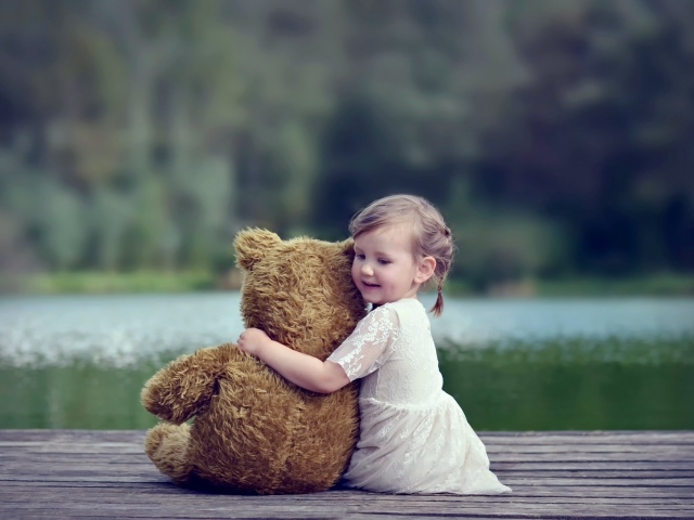 Маленькая девочка в белом платье сидит на мосту с плюшевым медведем