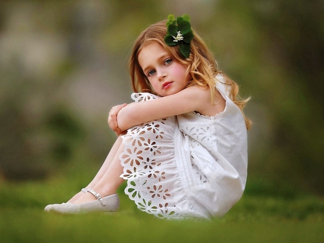 Маленькая девочка в белом платье сидит на зеленой траве
