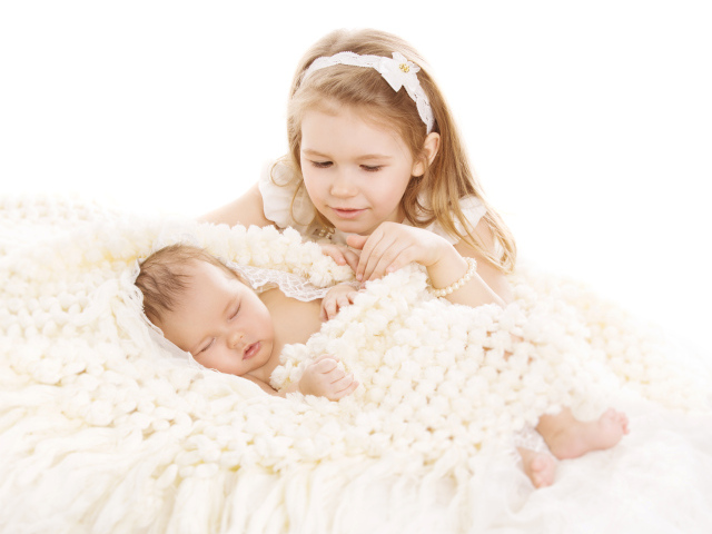 Маленькая девочка в белом со спящим младенцем на белом фоне
