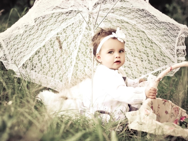 Маленькая девочка сидит на траве с большим белым зонтом