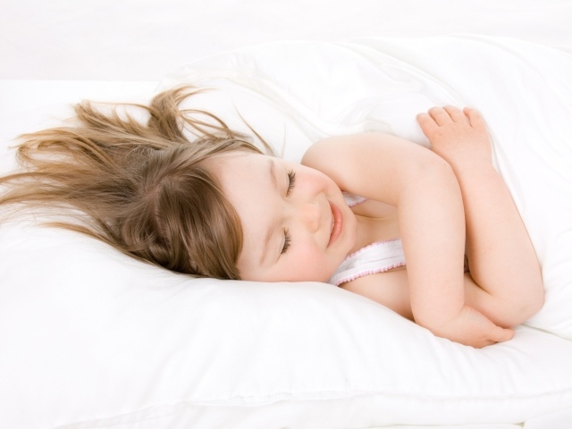 Маленькая девочка спит на белой кровати