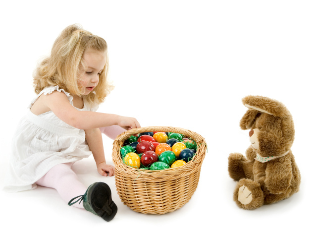 Маленькая девочка с корзиной пасхальных яиц и игрушкой на белом фоне