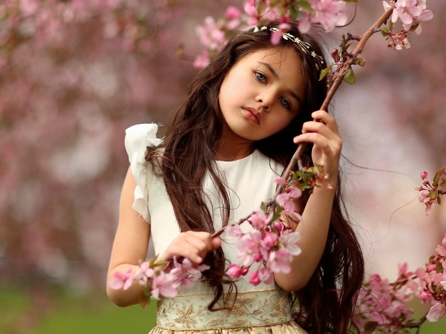 Маленькая девочка у цветущей розовыми цветами ветки