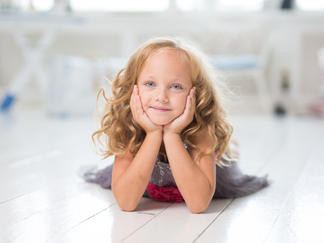 Маленькая длинноволосая голубоглазая девочка лежит на полу