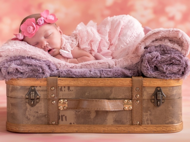 Маленькая новорожденная девочка спит на чемодане