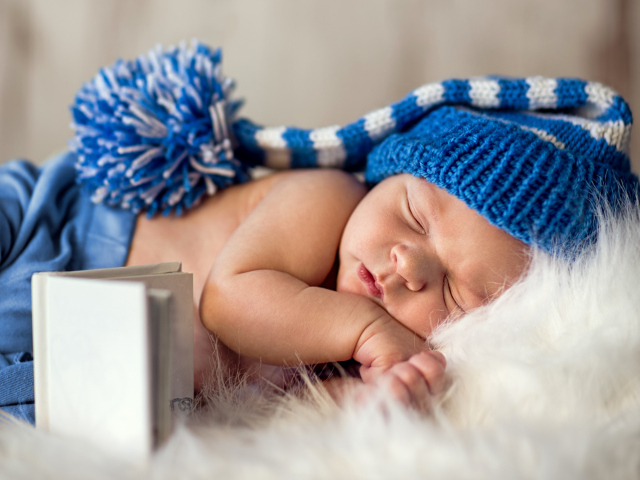 Маленький спящий грудной ребенок в синей вязанной шапке 