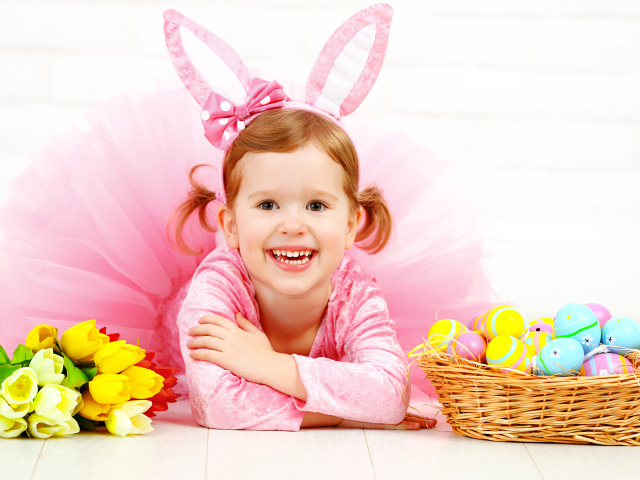 Маленькая улыбающаяся девочка в розовом с пасхальными яйцами и букетом тюльпанов