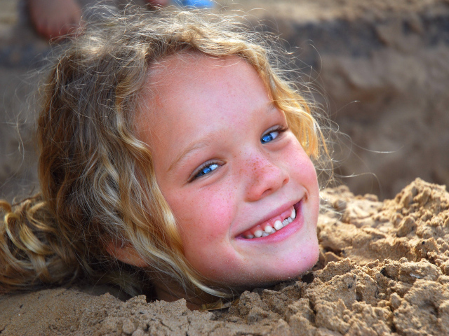 Маленькая улыбающаяся девочка играет в песке