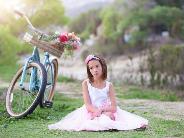 Грустная девочка в красивом платье сидит на траве с велосипедом