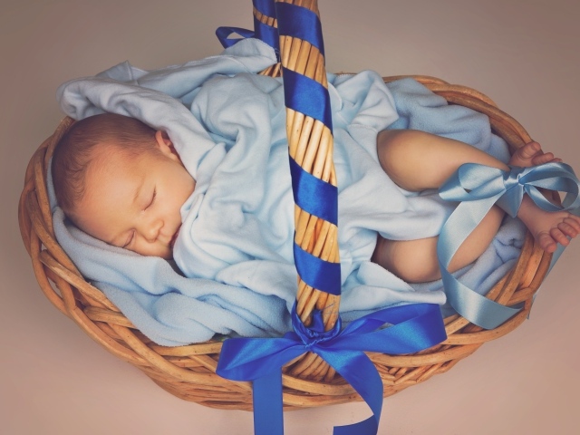 Спящий грудной ребенок в корзине с синими лентами