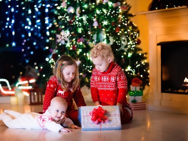 Маленькие дети с новогодним подарком у наряженной елки