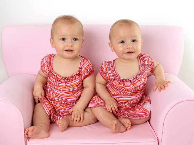 Две милые маленькие девочки сидят на розовом диване