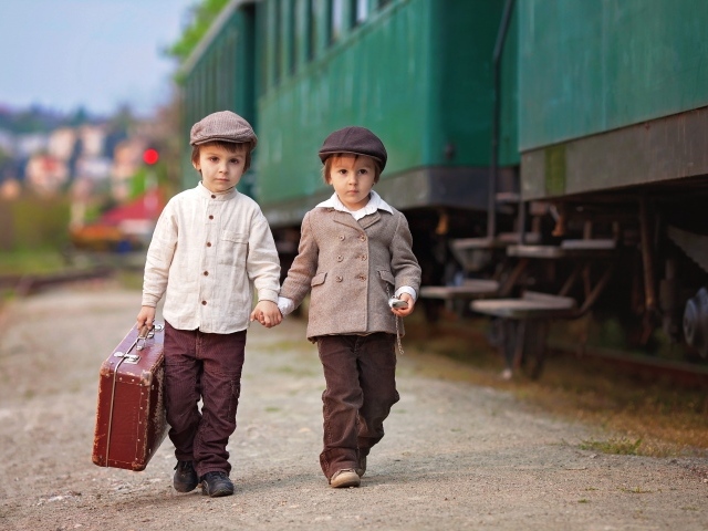 Два маленьких мальчика с большим чемоданом у поезда