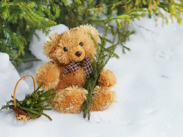 Медвежонок Тедди с веткой ели сидит на снегу