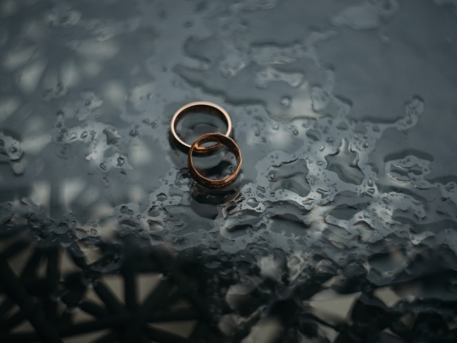 Два обручальных кольца лежат на мокрой черной поверхности 