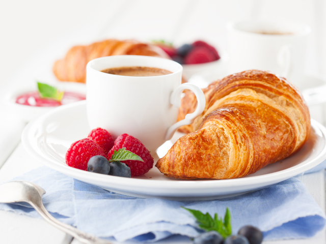 Чашка кофе на тарелке с круассаном и ягодами
