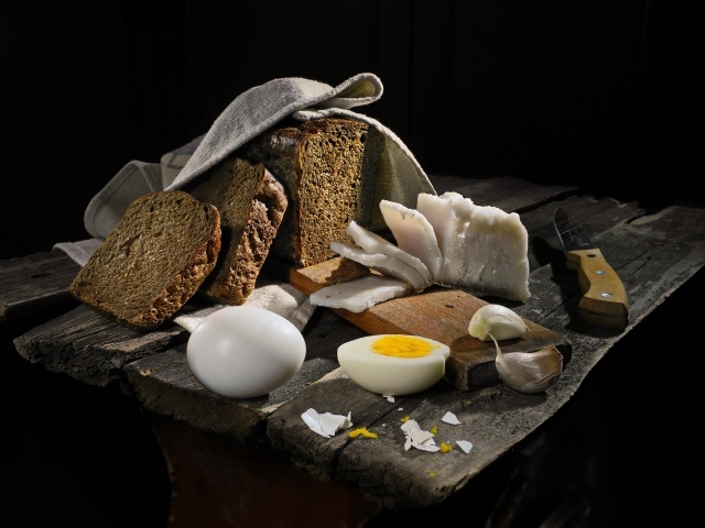 Черный хлеб, вареные яйца, чеснок и сало на деревянном столе