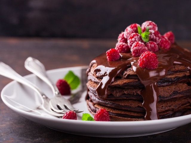 Шоколадные оладьи на тарелке с шоколадом и ягодами малины 
