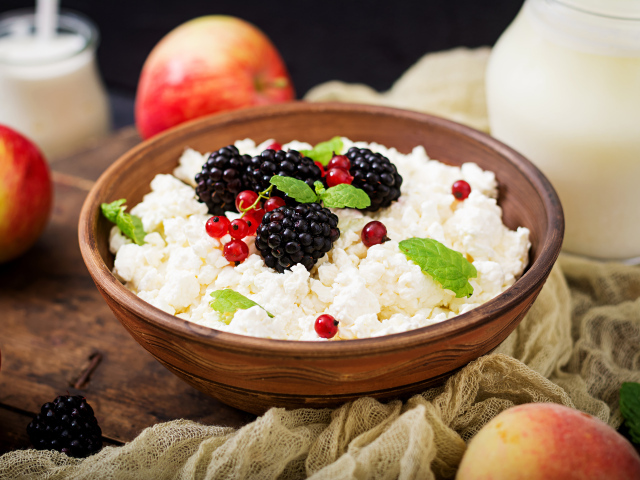 Творог с ягодами в деревянной миске на столе с яблоками