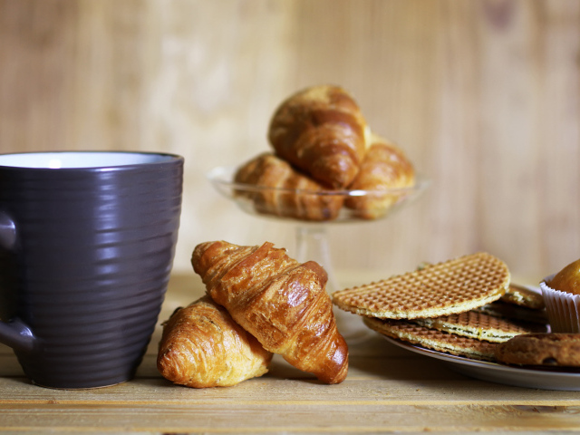 Чашка на столе с круассанами и вафлями 