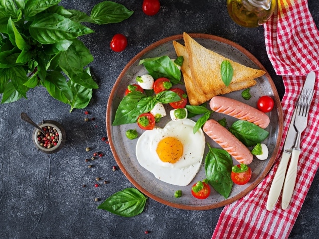 Яичница на тарелке с помидорами, гренками, сыром, сосисками и зеленью базилика