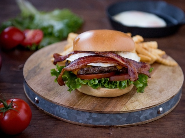 Гамбургер с беконом на столе с овощами