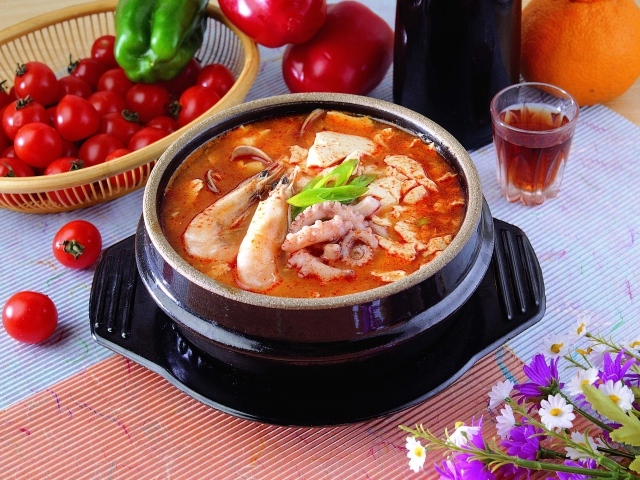 Тарелка красного супа с морепродуктами на столе с овощами 