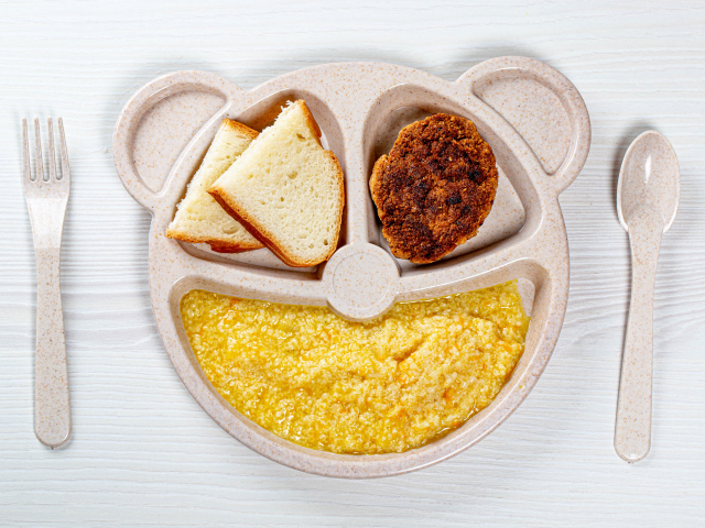 Каша на тарелке с котлетой и хлебом для ребенка