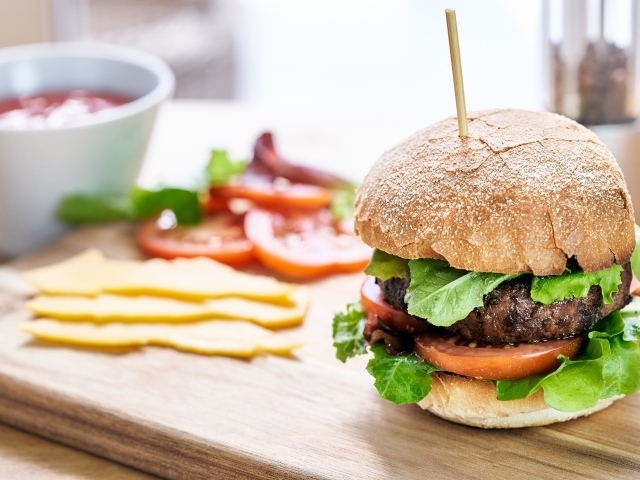 Аппетитный гамбургер на доске с сыром и помидорами