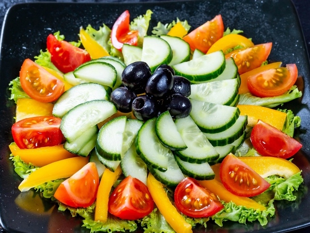 Салат из помидоров, огурцов и перца на тарелке с листьями салата и оливками