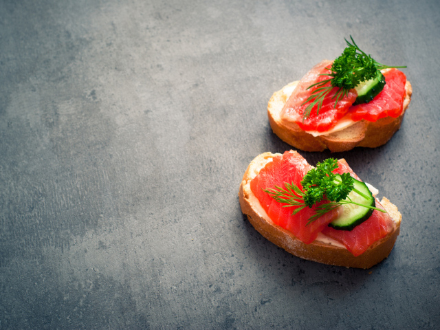 Два бутерброда с красной рыбой, огурцом и зеленью на черном фоне