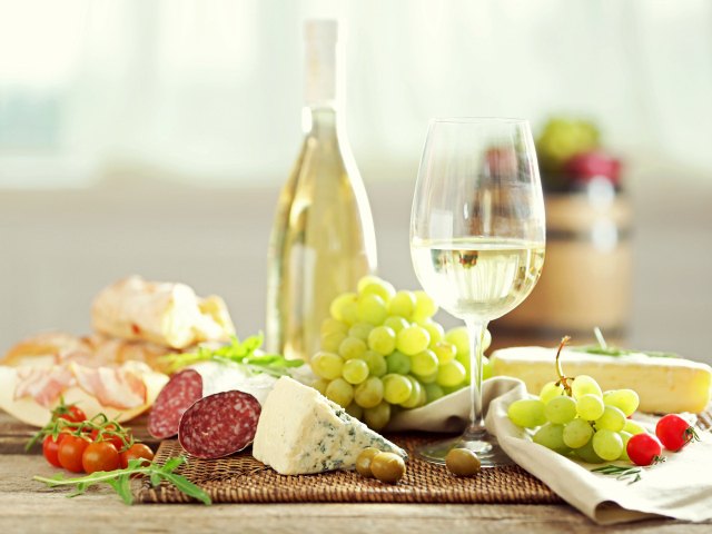 Белое вино на столе с сыром, колбасой и виноградом