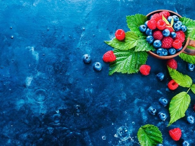 Чашка с ягодами черники и малины на синем столе
