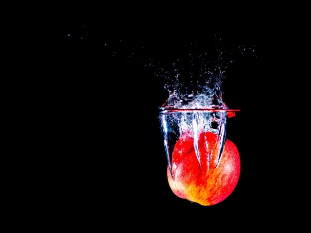 Красное яблоко падает в воду на черном фоне