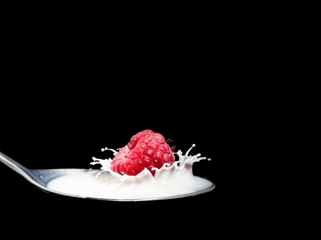 Спелая красная малина с ложке с молоком на черном фоне