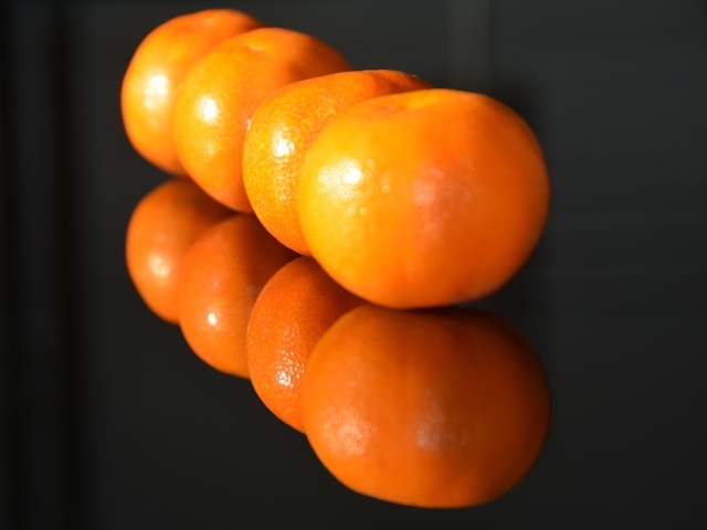 Желтые мандарины отражаются в поверхности стола 