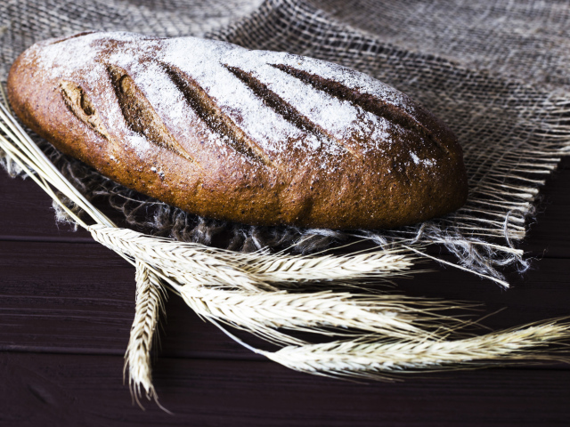 Буханка свежего хлеба на столе с колосьями пшеницы