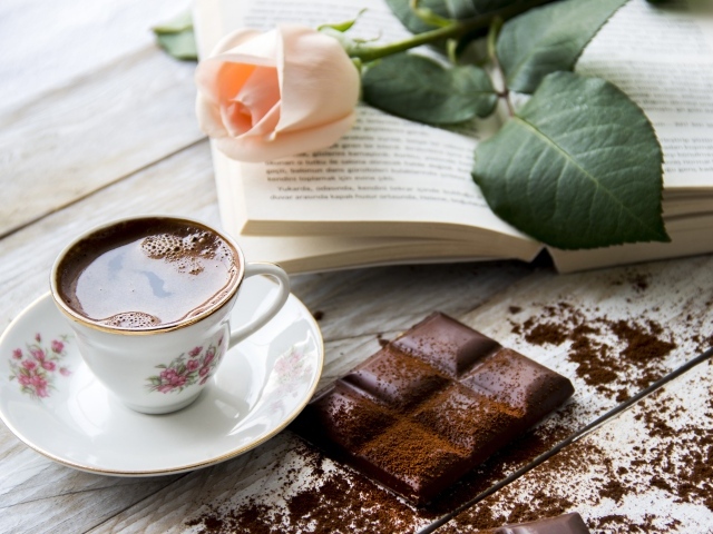 Чашка кофе на столе с шоколадом, книгой и розой