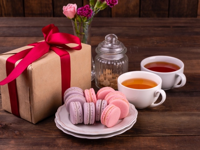 Подарок с красной лентой на столе с макарунами и чаем 