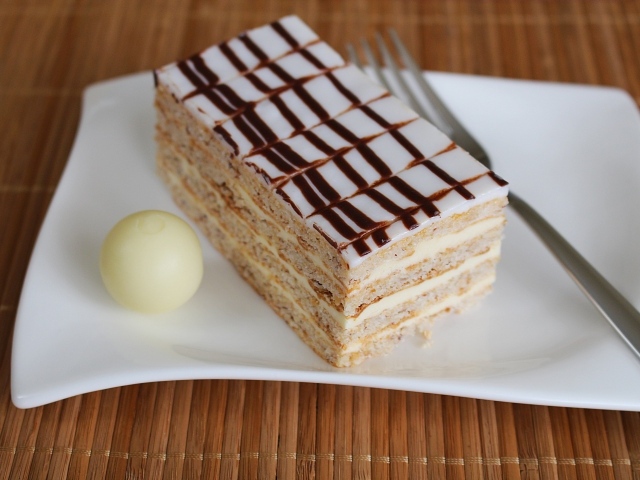 Кусок торта на белой тарелке с вилкой и конфетой 