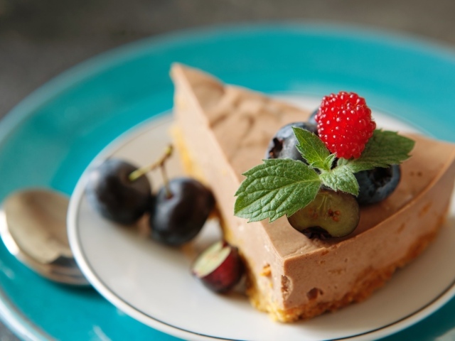 Кусок чизкейка на тарелке с ягодами черники и малиной