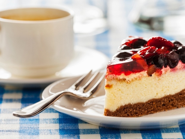 Кусок чизкейка с ягодами и желе на столе с чашкой кофе